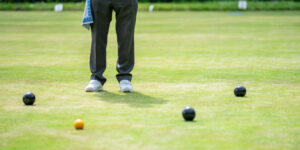 Pair of legs with 3 bowls and jack on bowling green.
